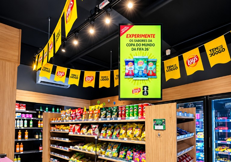 Tela digital com anúncio em mercado, cercada por prateleiras